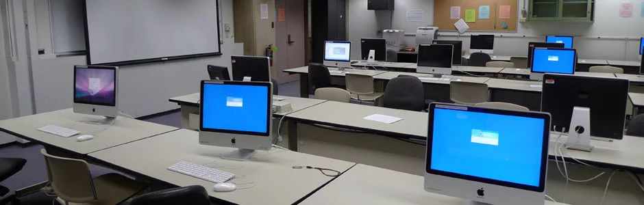 A classroom with a computer monitor and keyboard at each seat.