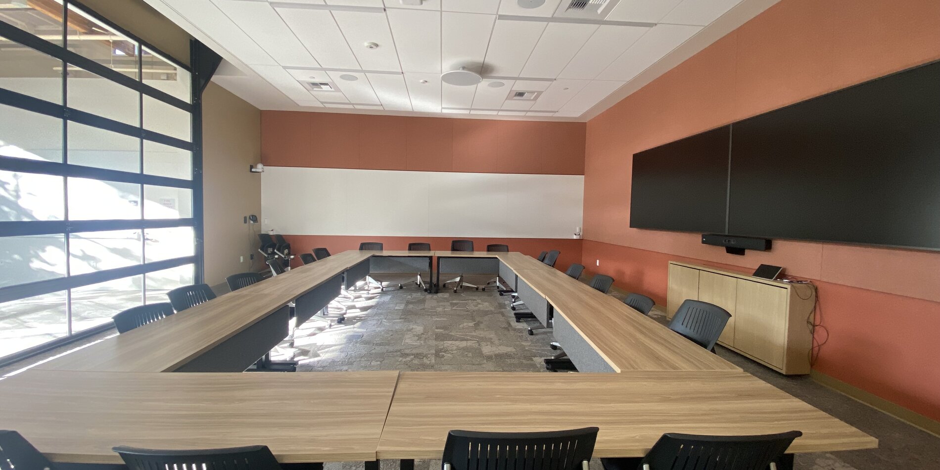 A large conference room with multiple displays on one wall and a retractable "garage" door on the other